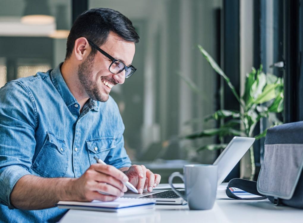 Businessman holding a pen and smiling in front of a laptop