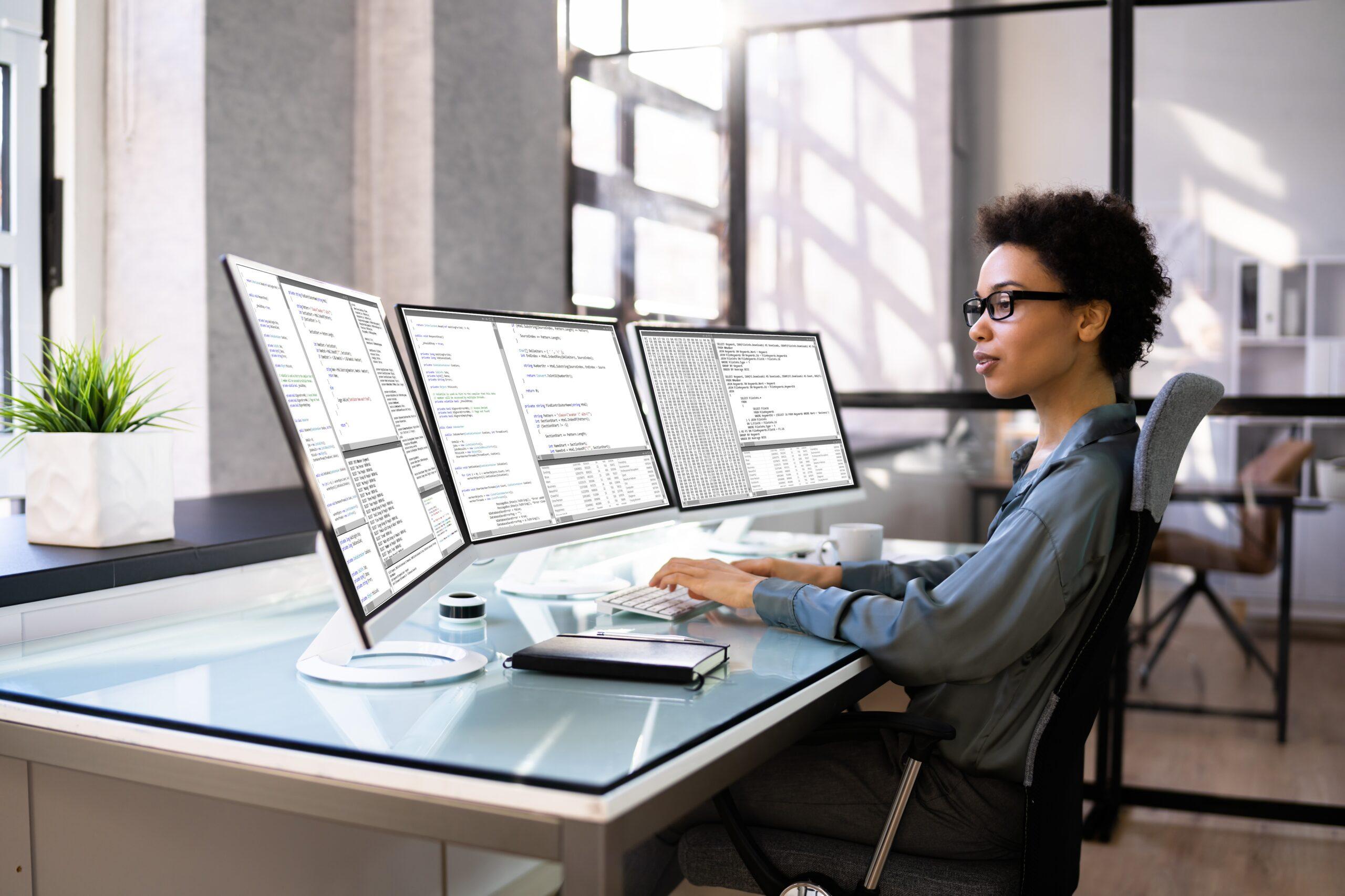 A woman types with three monitors in front of her