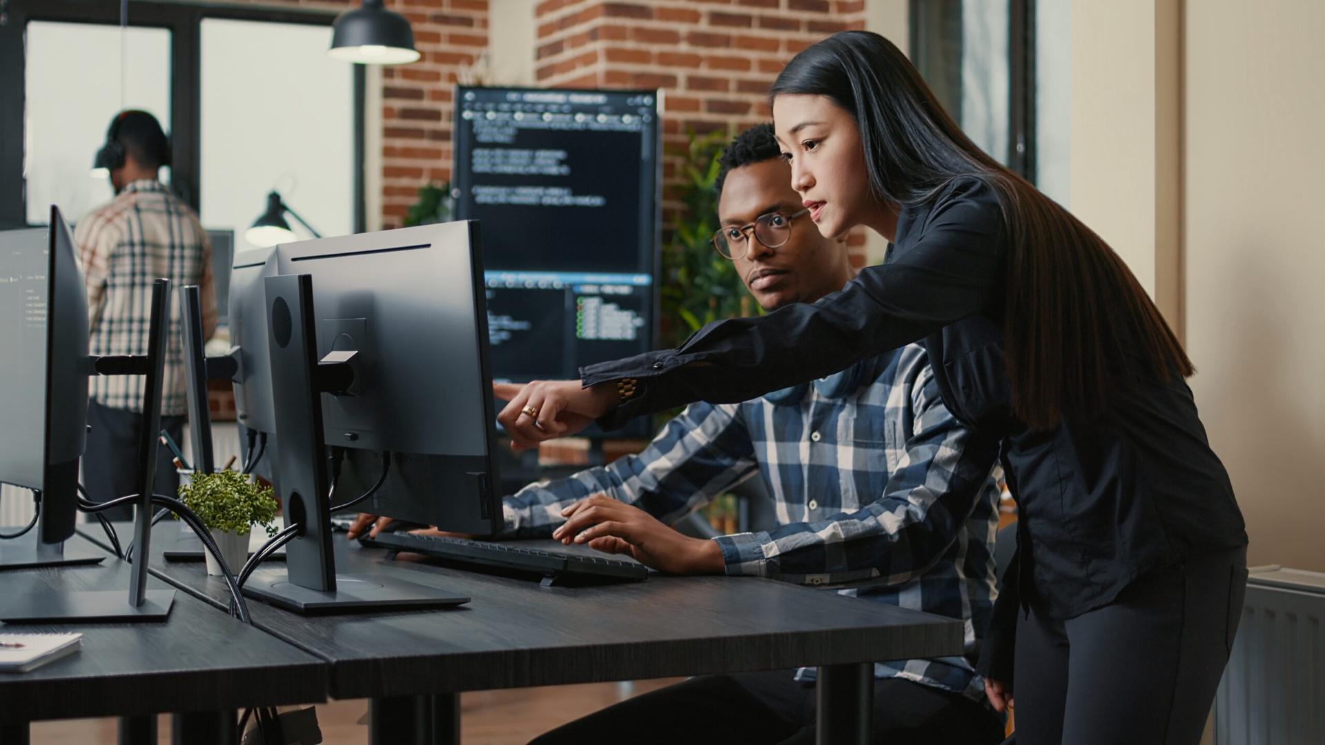 A woman stands over a man's shoulder pointing at his computer screen