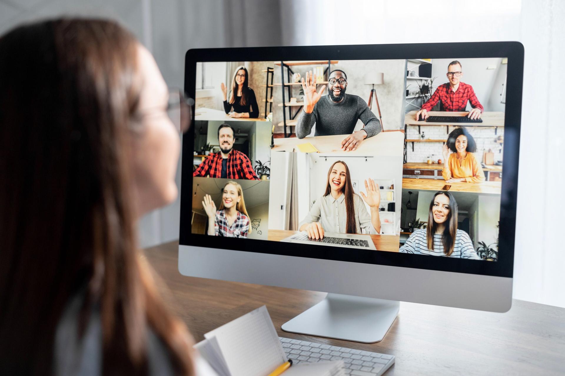 Shot from the side of a woman's face, looking at a computer monitor with an array of faces in a videoconferencing meeting