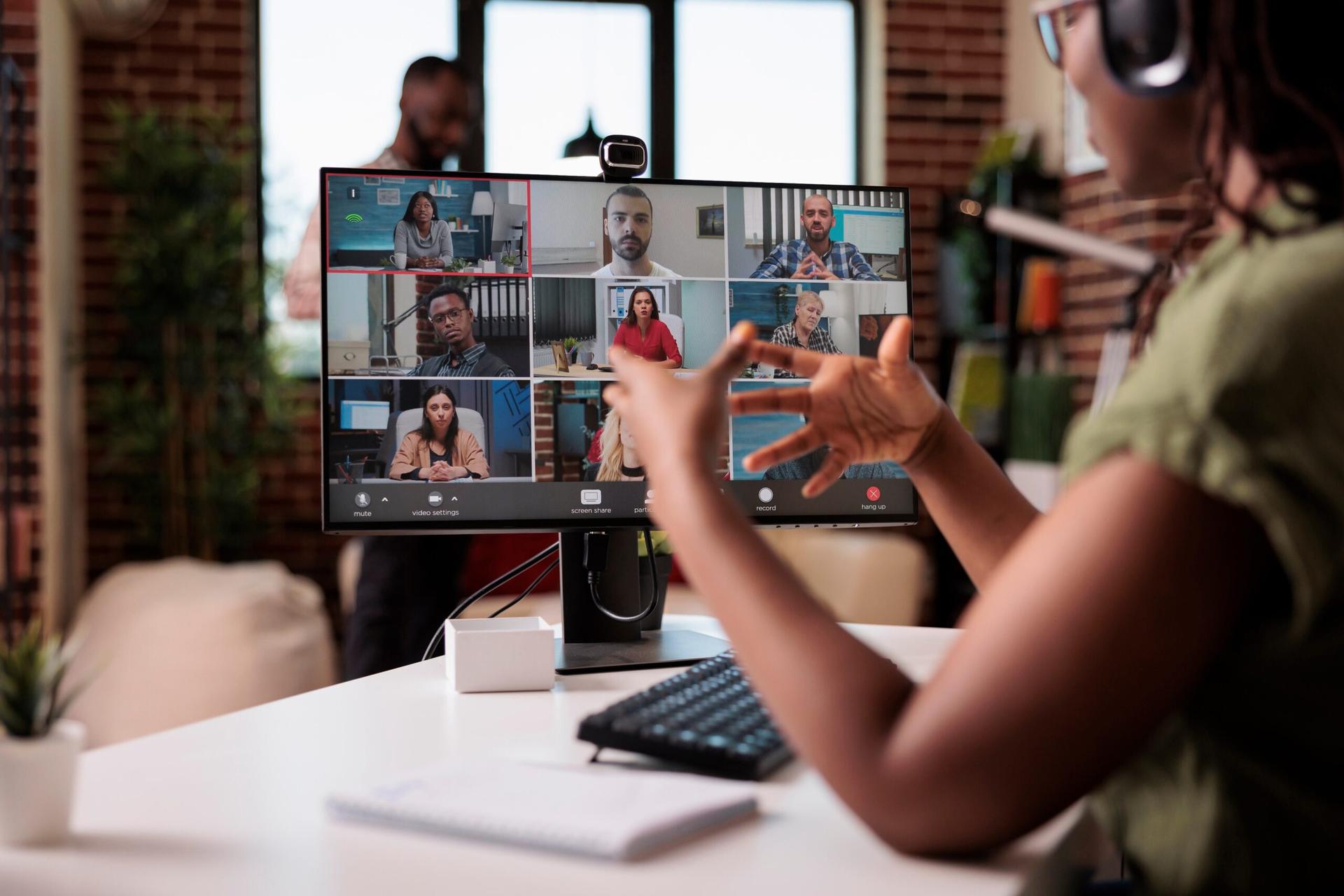 Employee working from home gesturing in video conference with colleagues at desk.